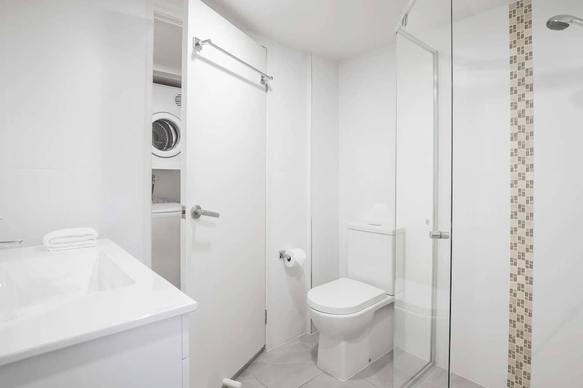 A modern bathroom with a glass shower enclosure, a toilet, and a built-in washing machine.