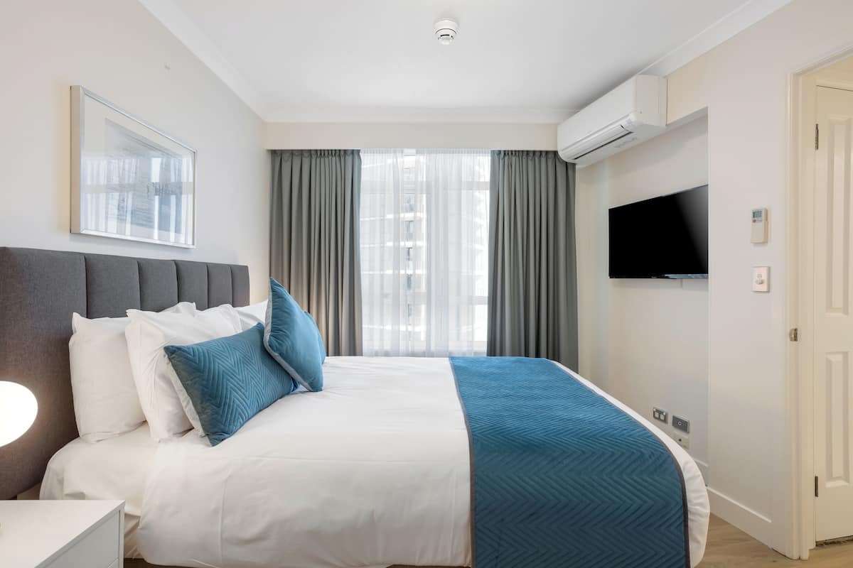 Habitación de hotel con cama, televisión, aire acondicionado y ventana con cortinas.