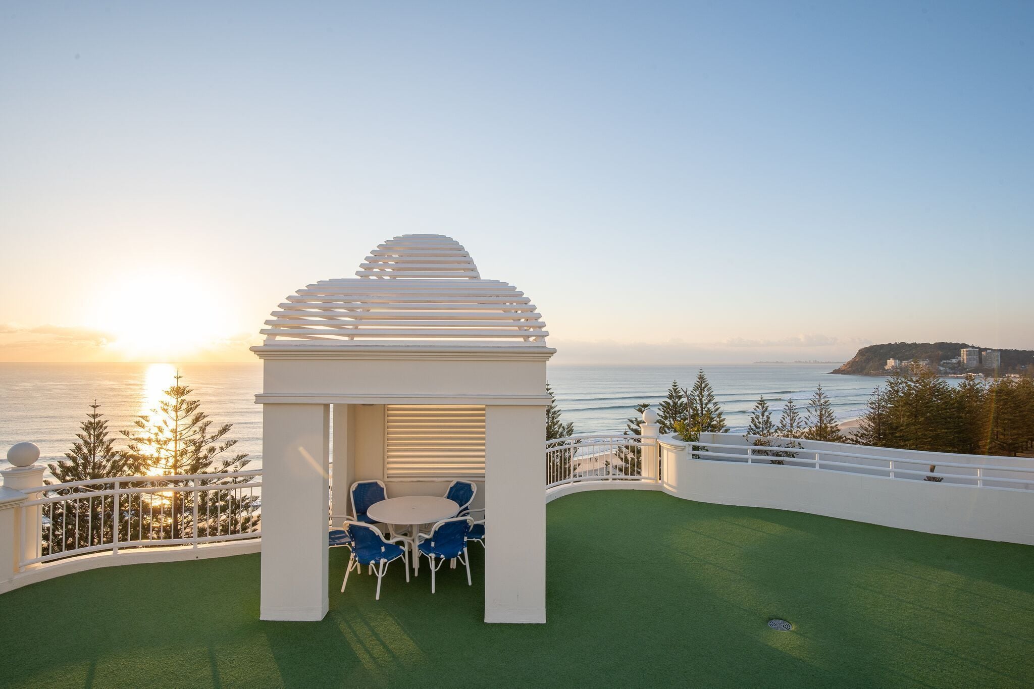 A white gazebo with blue chairs on a green lawn overlooking the sea.