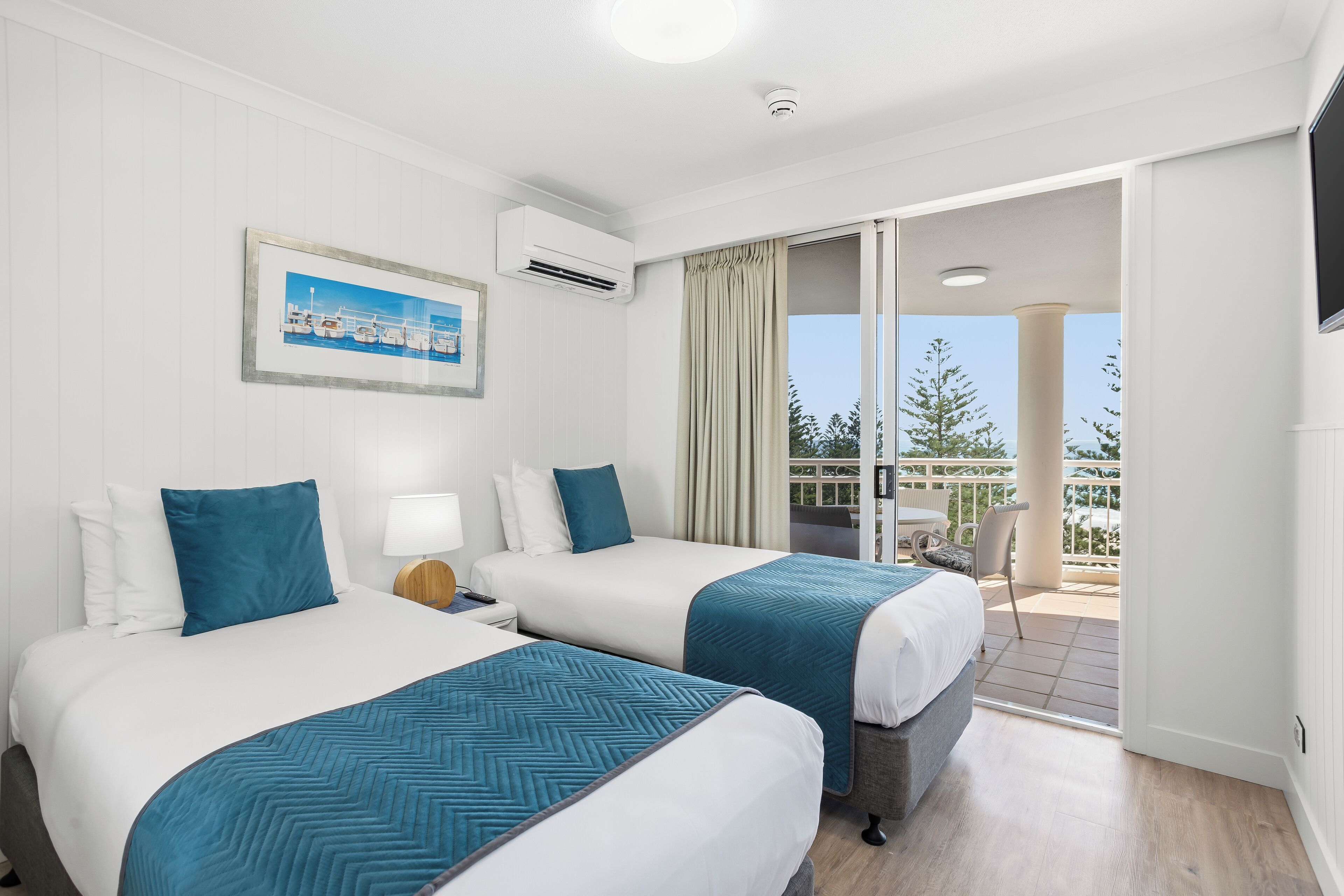 Habitación de hotel con dos camas, televisión, aire acondicionado y balcón con mesa y sillas.