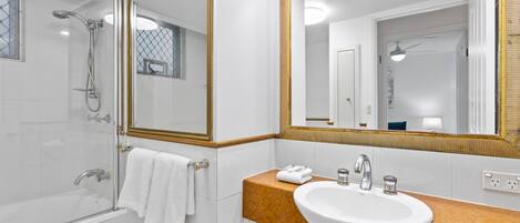 Un baño moderno con ducha de vidrio, un lavamanos blanco con encimera de mármol y un espejo grande con marco dorado.