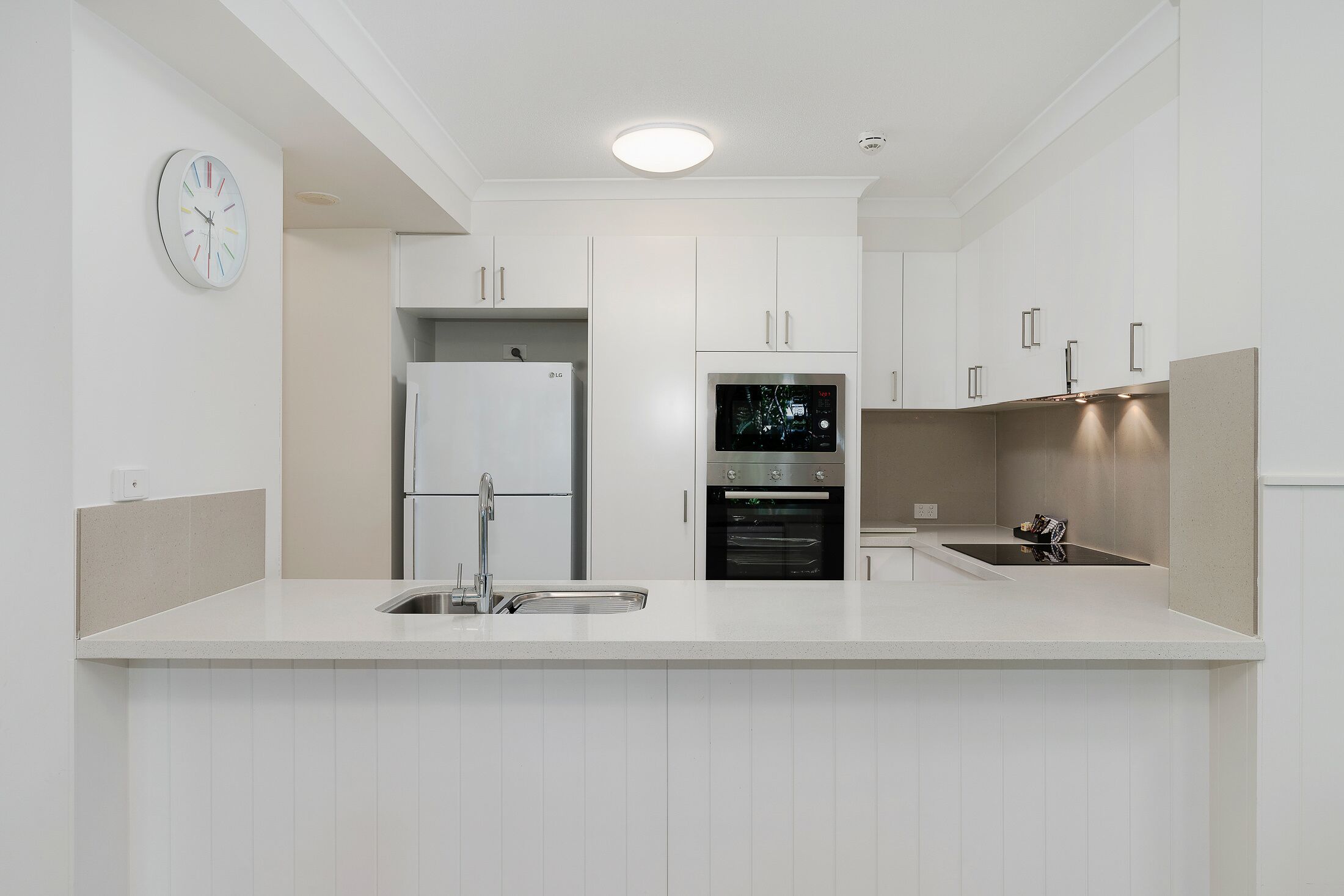 A modern kitchen with white cabinetry, a built-in oven, and a stainless steel refrigerator.