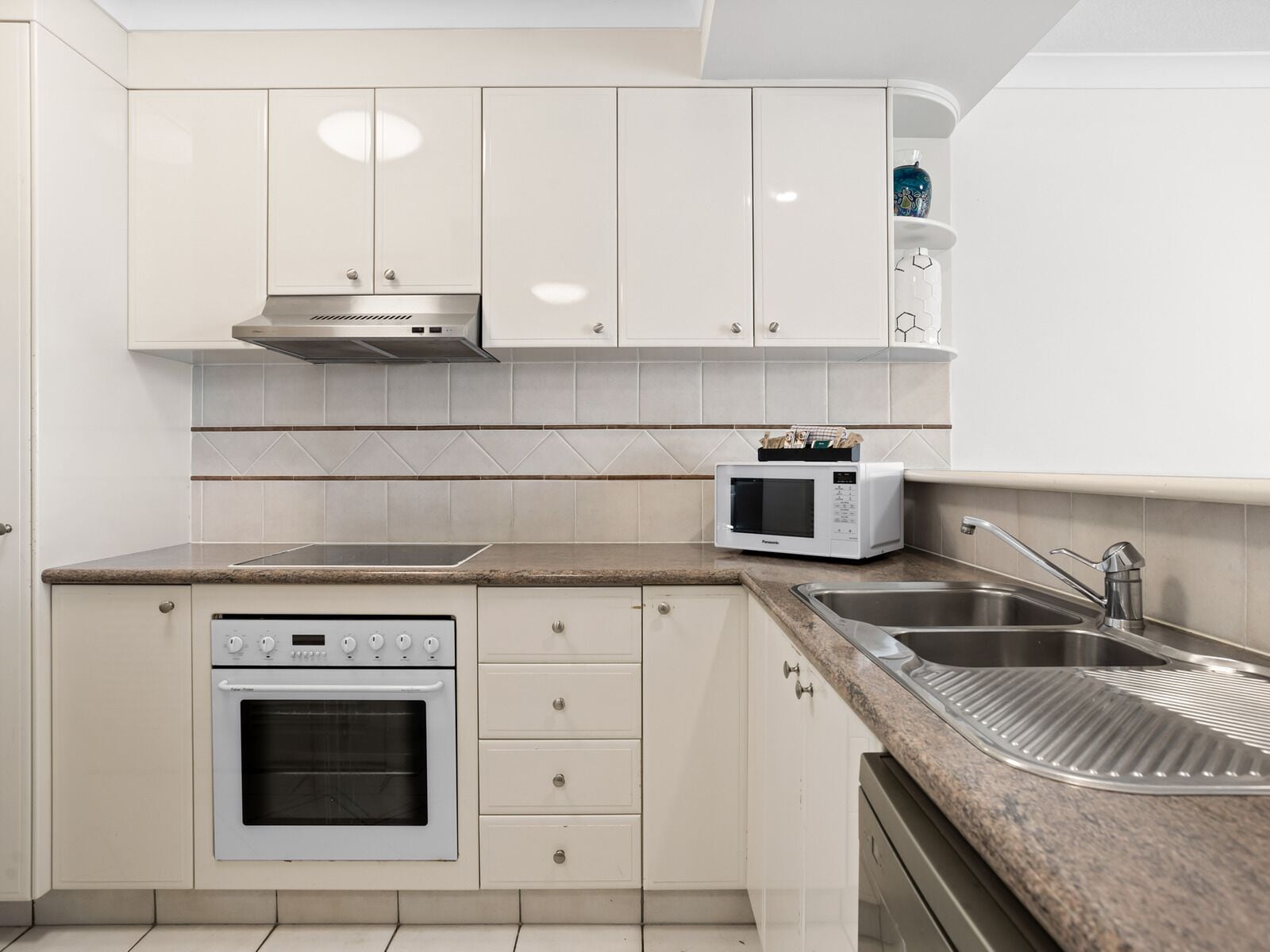 Una cocina moderna con armarios blancos, un lavamanos de acero inoxidable, un microondas y un horno.