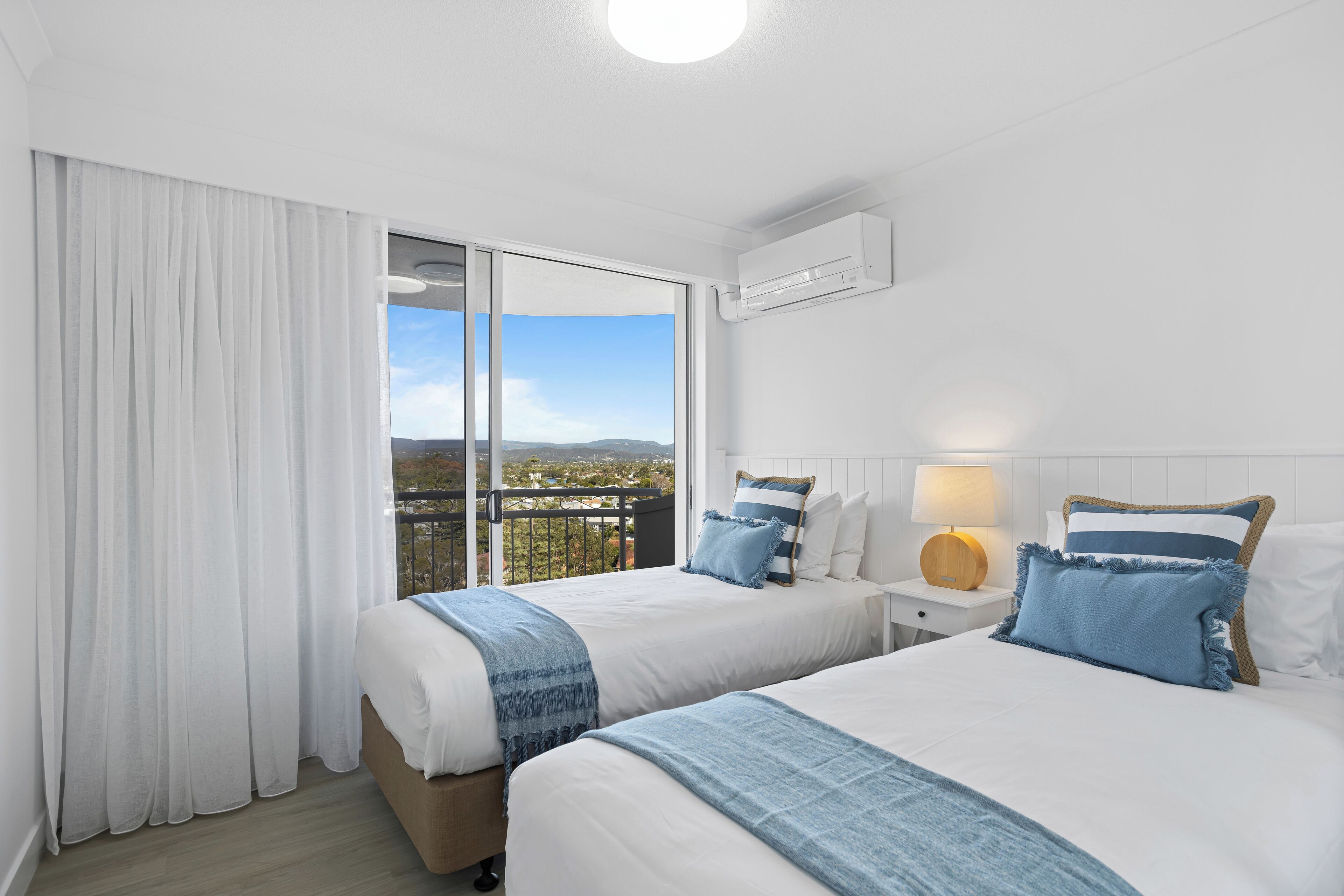 A hotel room with two beds, a balcony with a view, white walls, and a ceiling fan.