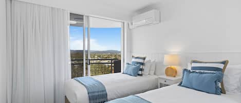 A hotel room with two beds, a balcony with a view, white walls, and a ceiling fan.