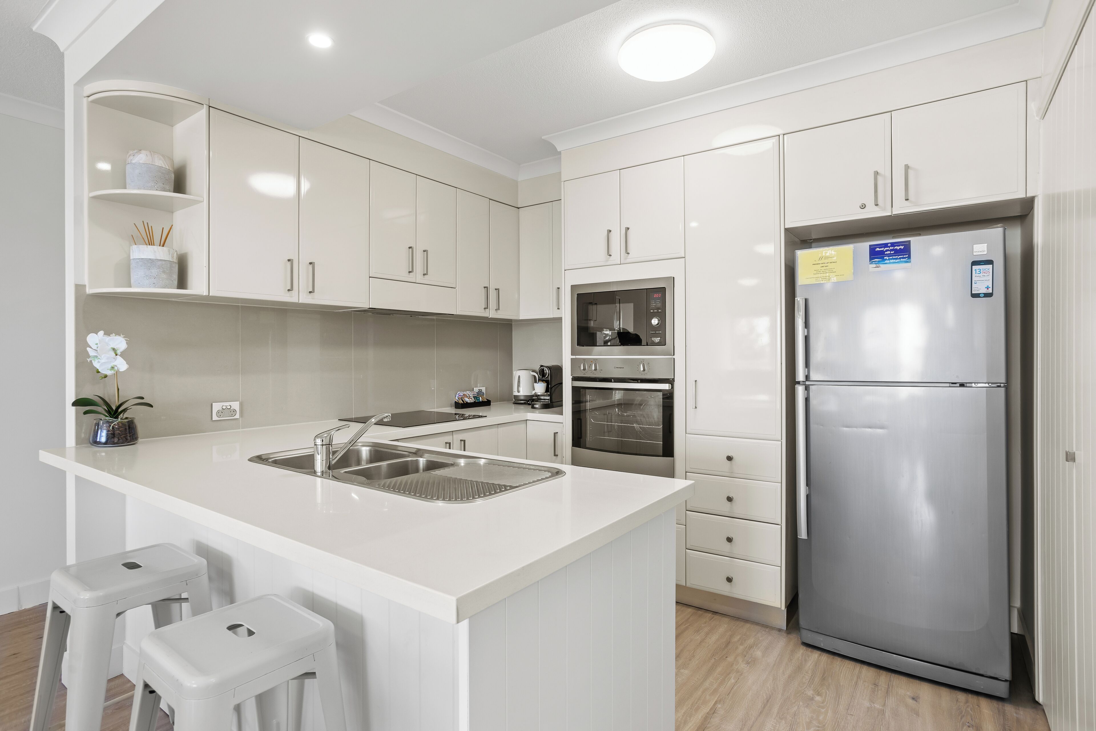 Una cocina moderna con armarios blancos, un refrigerador de acero inoxidable y un horno empotrado.