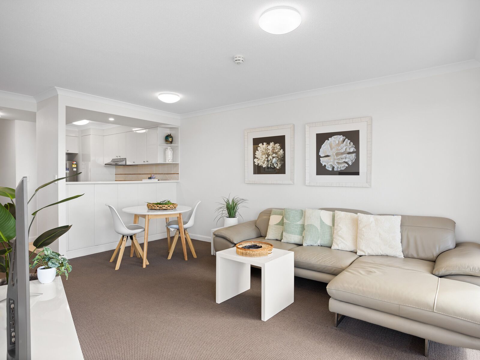 Una sala de estar moderna con un sofá color beige, una mesa de centro blanca y una zona de comedor con una mesa redonda y sillas.