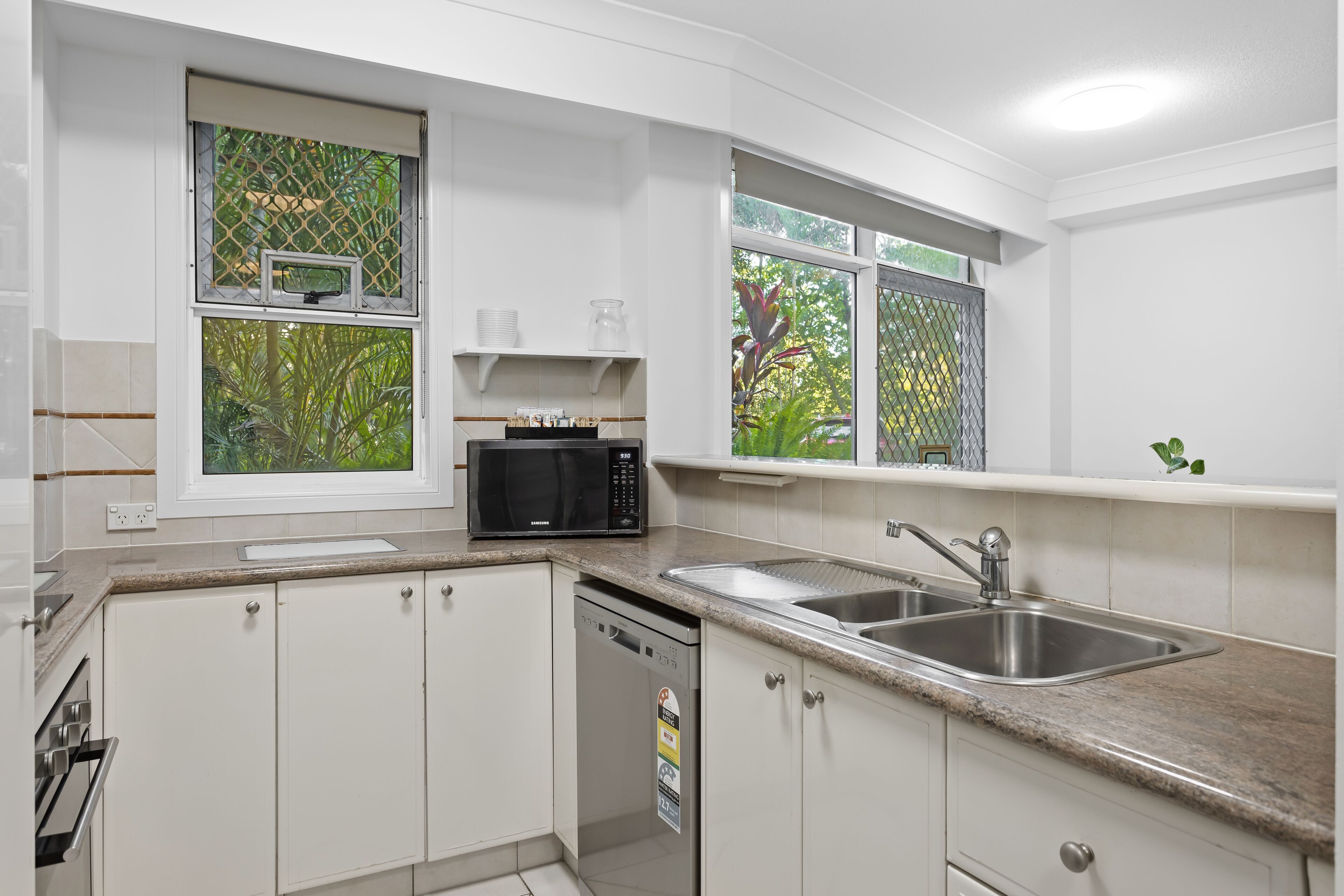 A modern kitchen with white cabinets, a stainless steel sink, a microwave, and a dishwasher.