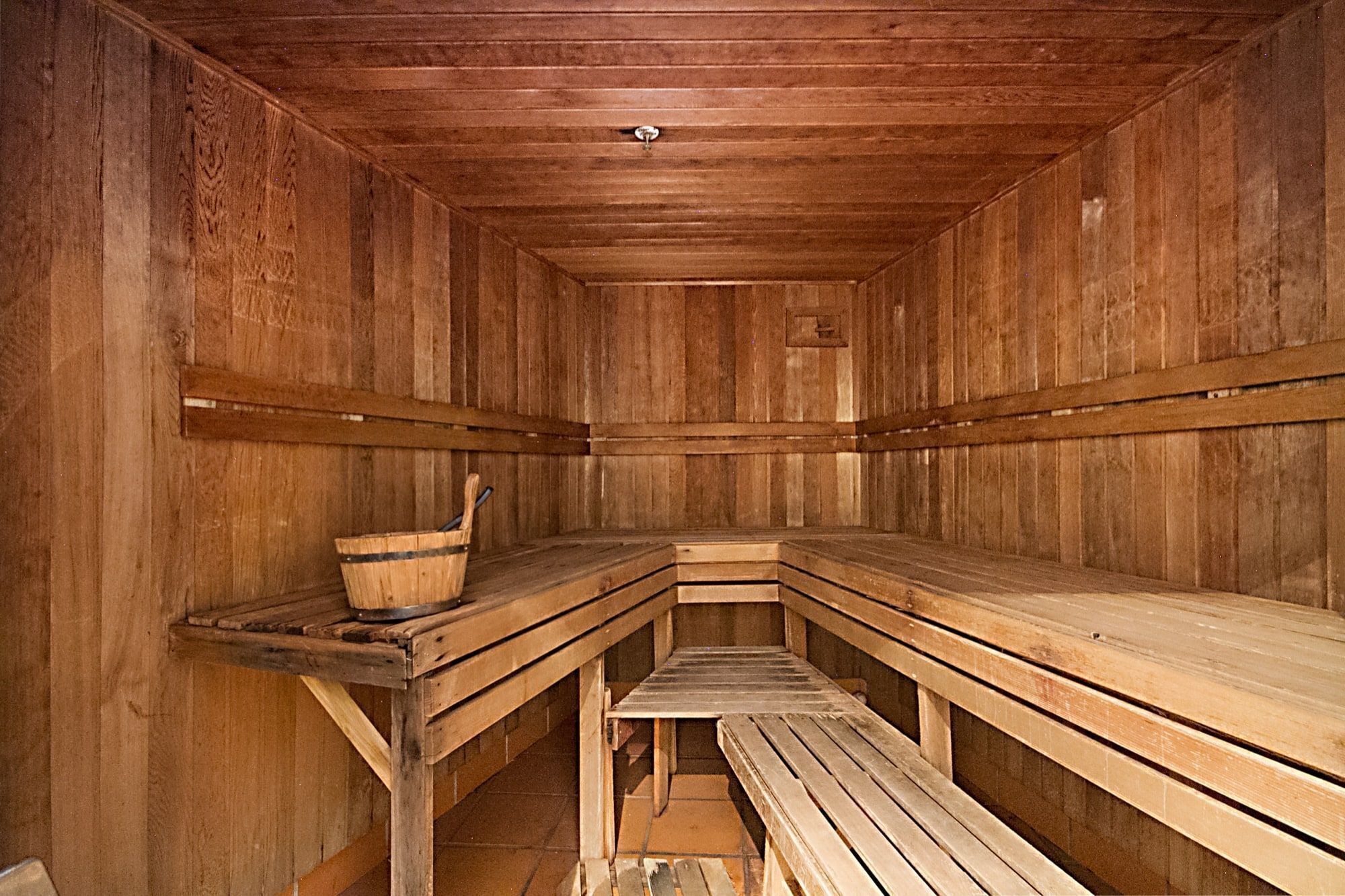Un sauna avec des bancs en bois et un seau en bois.