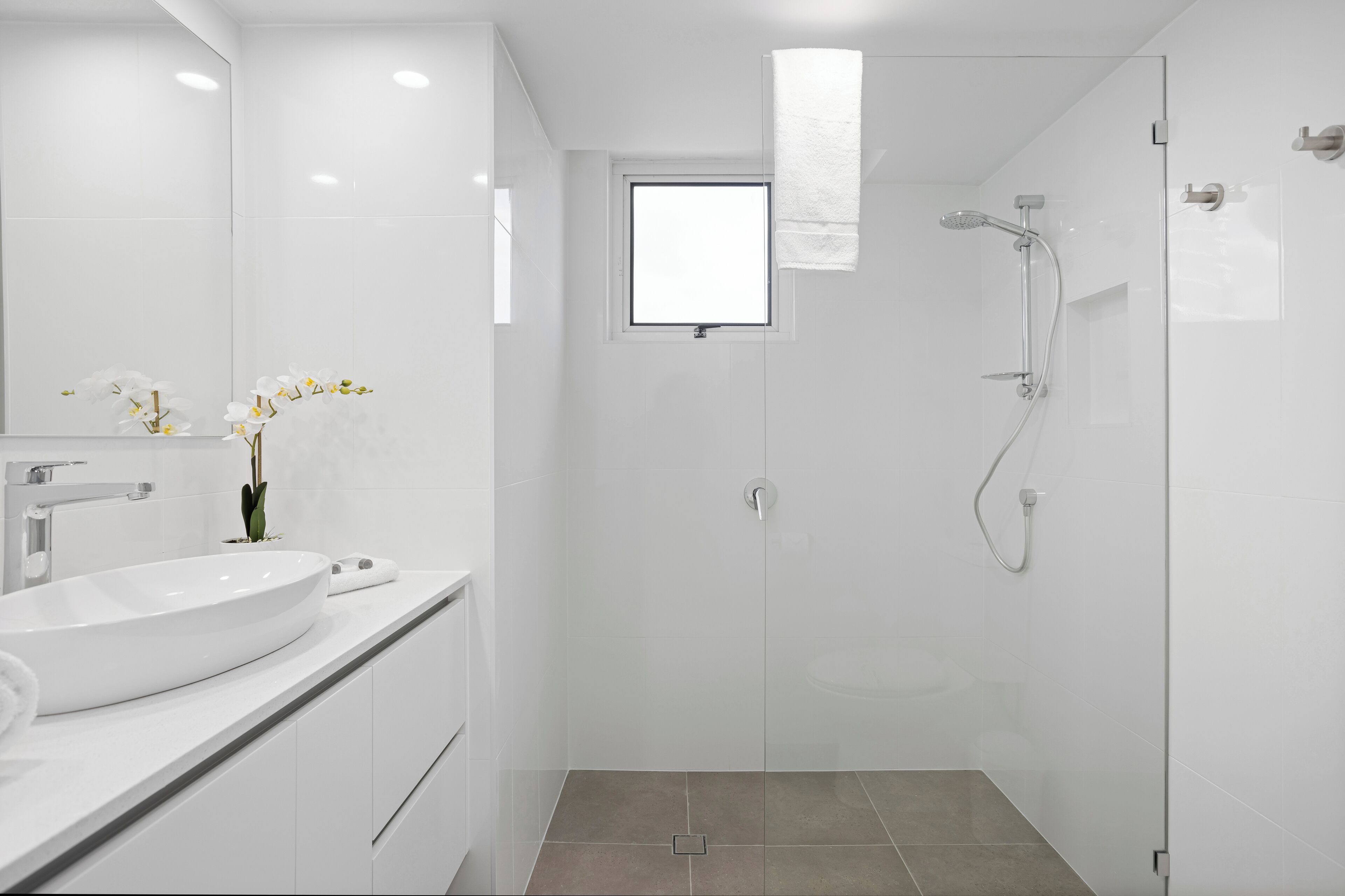 A modern bathroom with a large white sink, a glass shower enclosure, and a small window.