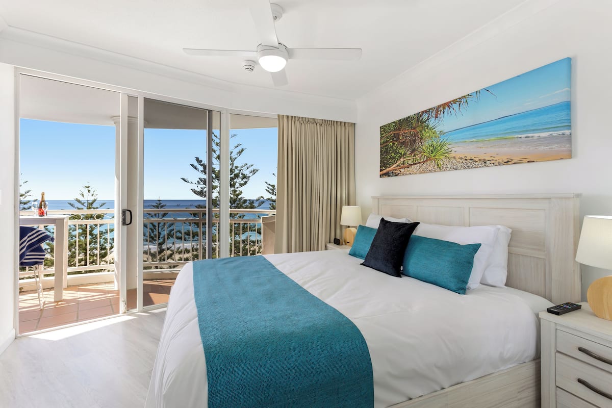 Un cuarto de hotel con una cama grande, un balcón con vista al mar y un ventilador de techo.