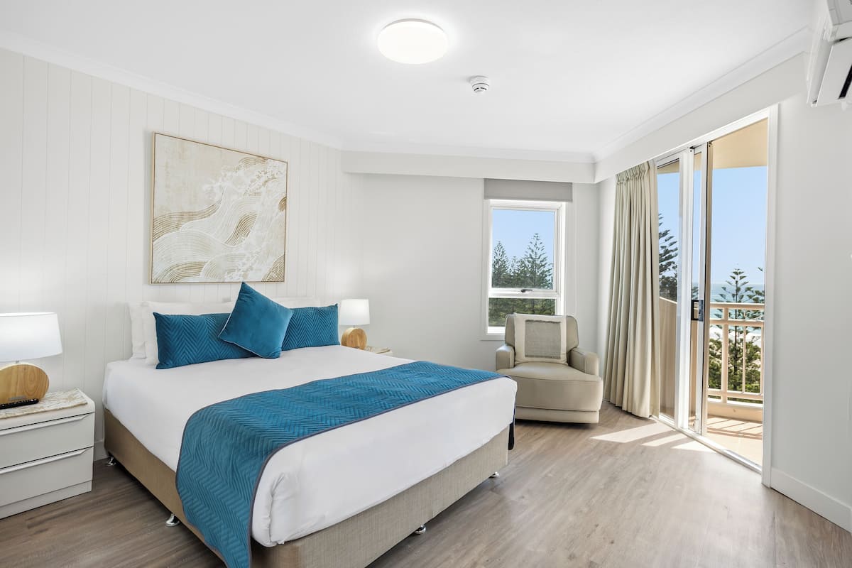 Un dormitorio moderno con una cama grande, una mesita de noche, una silla y un balcón con vistas.