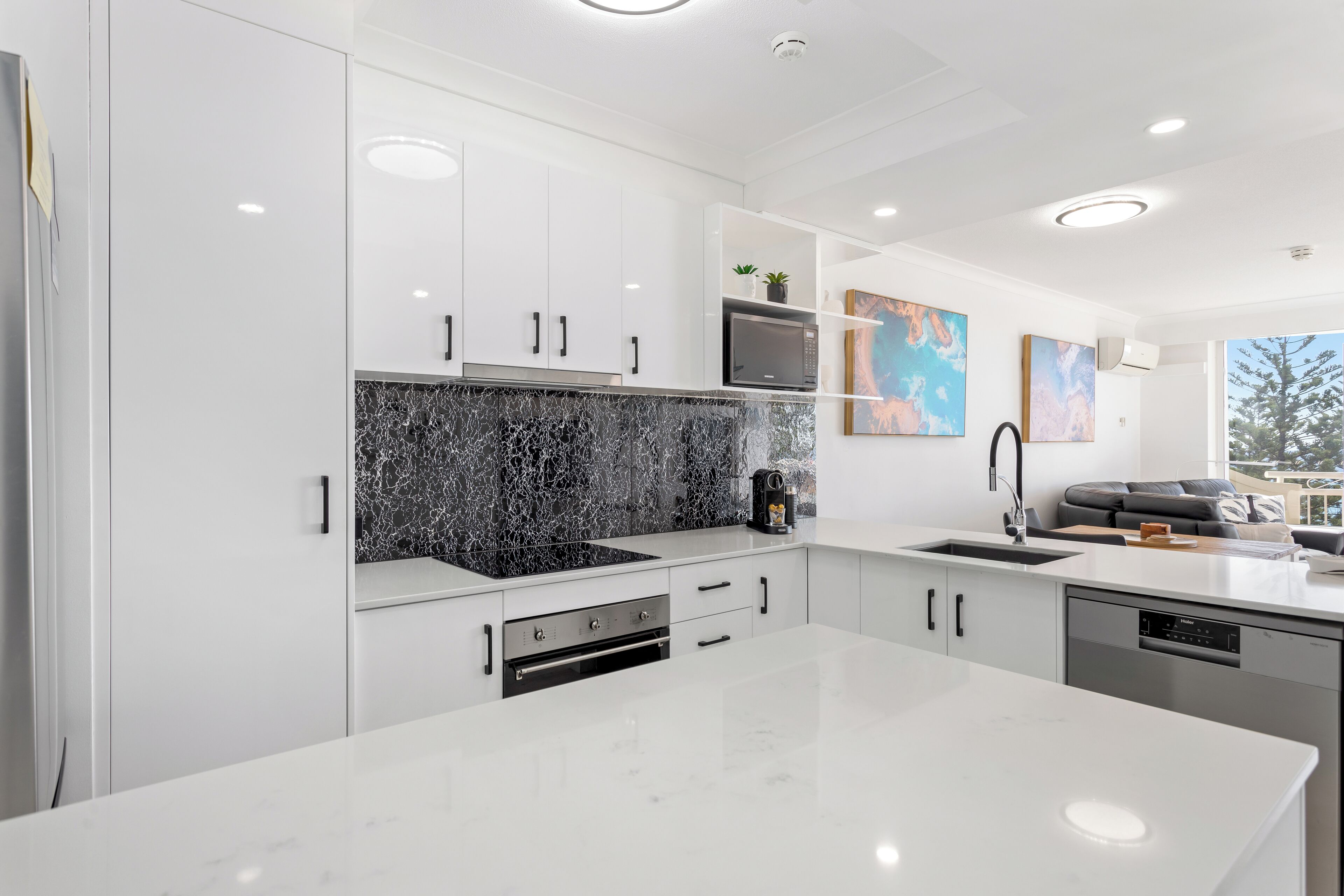 A modern kitchen with white cabinetry, a black marble backsplash, and a large island.