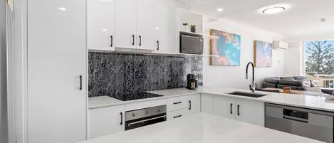 A modern kitchen with white cabinetry, a black marble backsplash, and a large island.