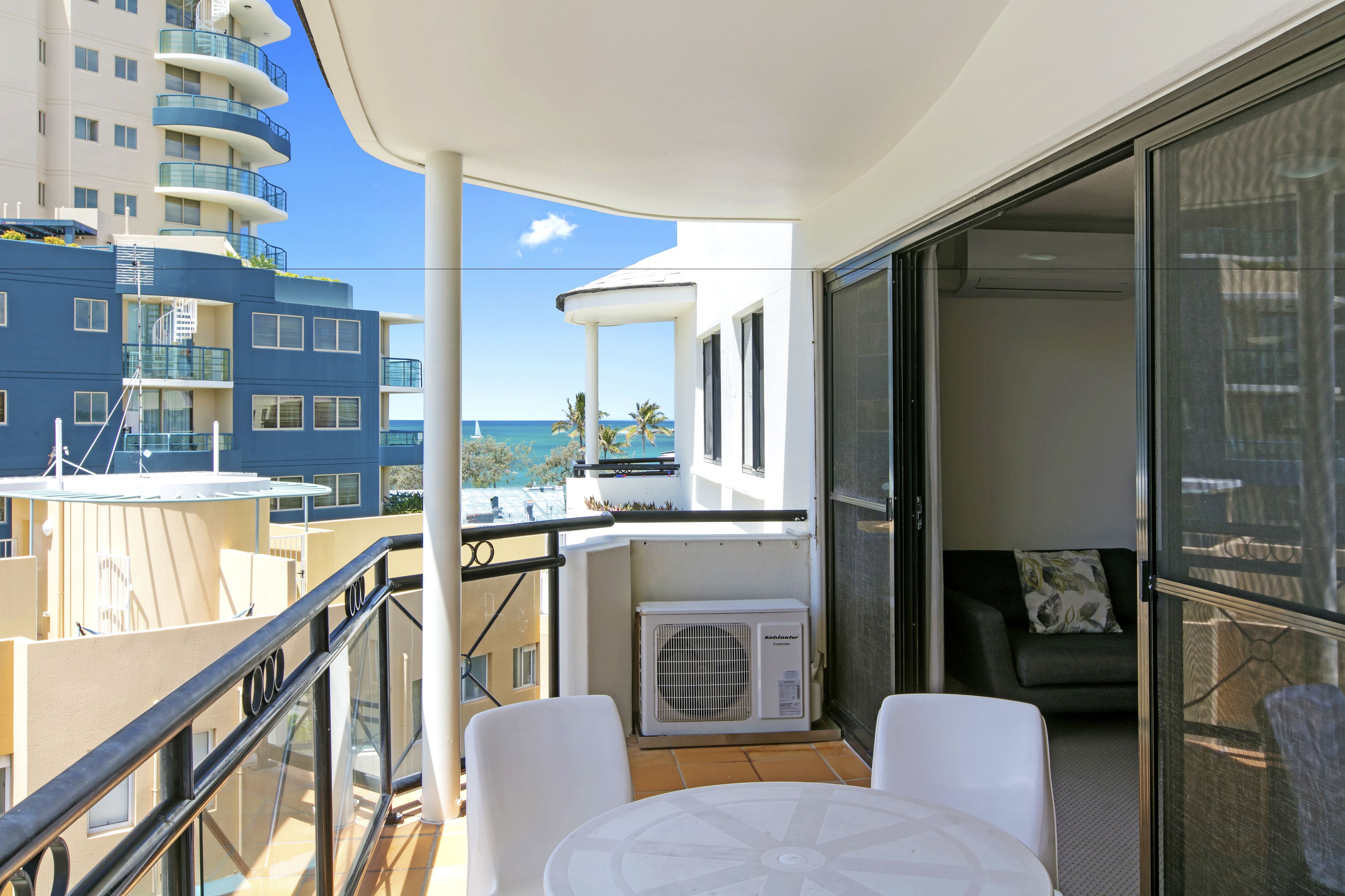 A balcony with a table and chairs, a view of the ocean, and a building in the background.