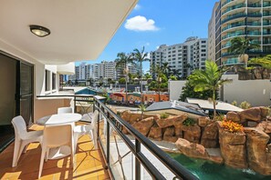 Varanda com piscina, cadeiras brancas e vista dos edifícios ao redor.