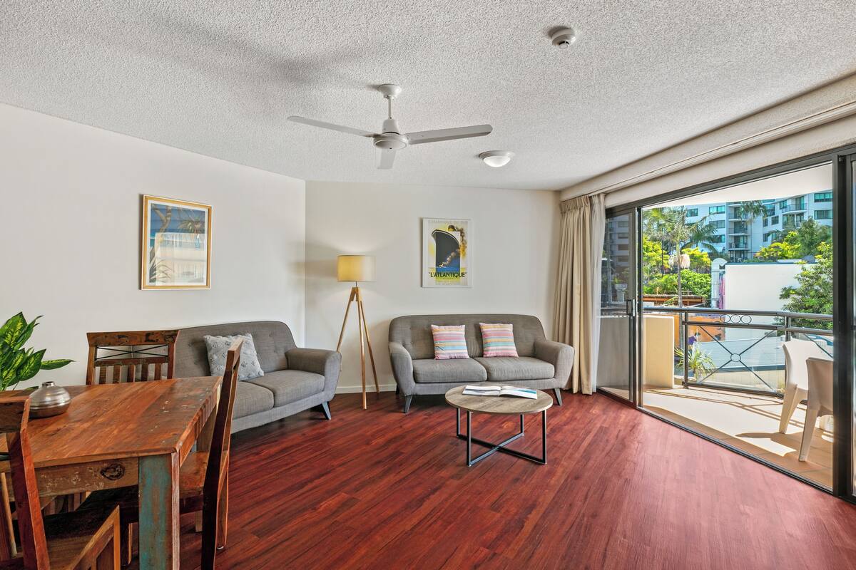 A spacious living area with a wooden dining table, two sofas, a coffee table, and a ceiling fan.