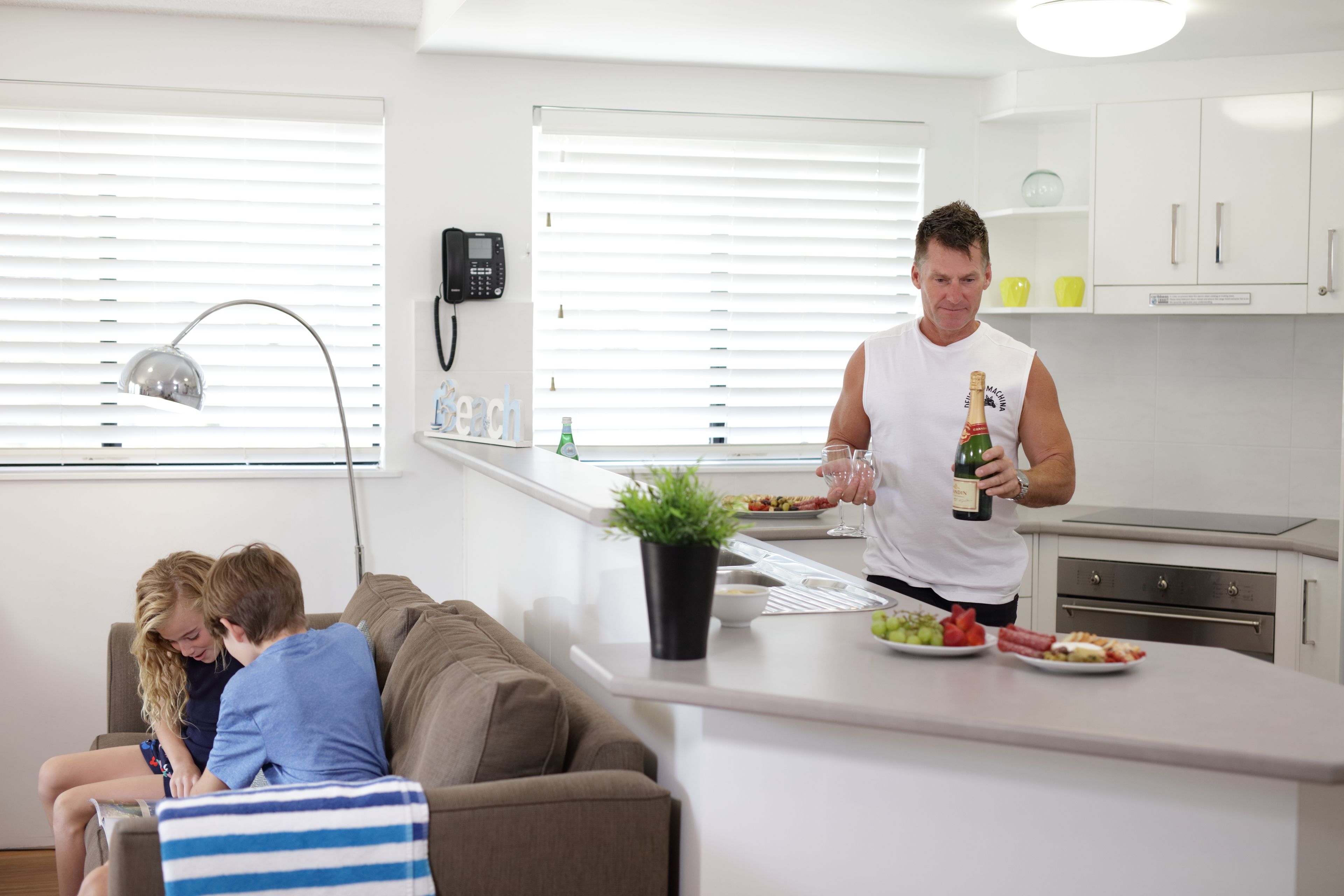 A modern kitchen with white cabinets, a countertop, and a dining area with a brown couch.