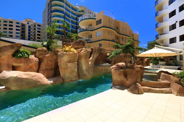 A hotel pool area with a rock formation and a clear blue pool.