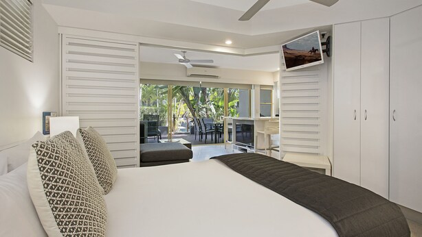 Ein Schlafzimmer mit Bett, Deckenventilator, Schreibtisch und Blick ins Freie.