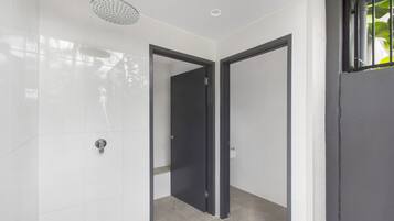 A modern bathroom with white tiles, a showerhead, and two doors leading to other rooms.