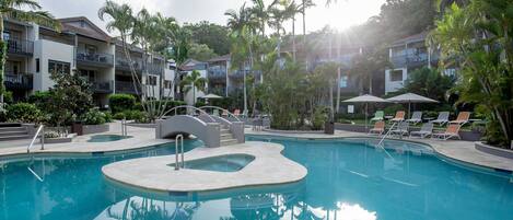 A swimming pool with lounge chairs and palm trees, surrounded by multi-story buildings with balconies.