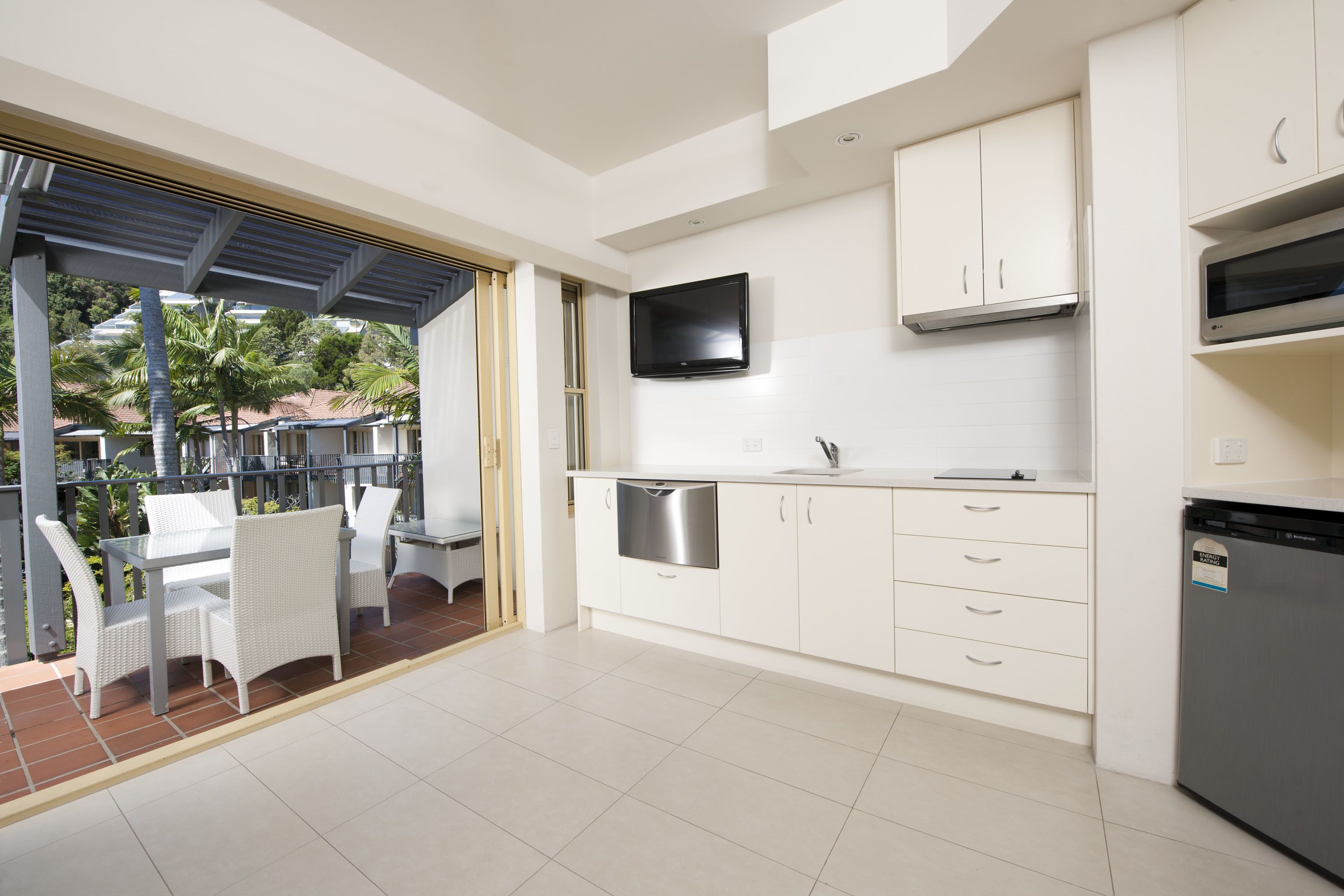 A modern kitchen with white cabinets, a built-in dishwasher, and a flat-screen TV.