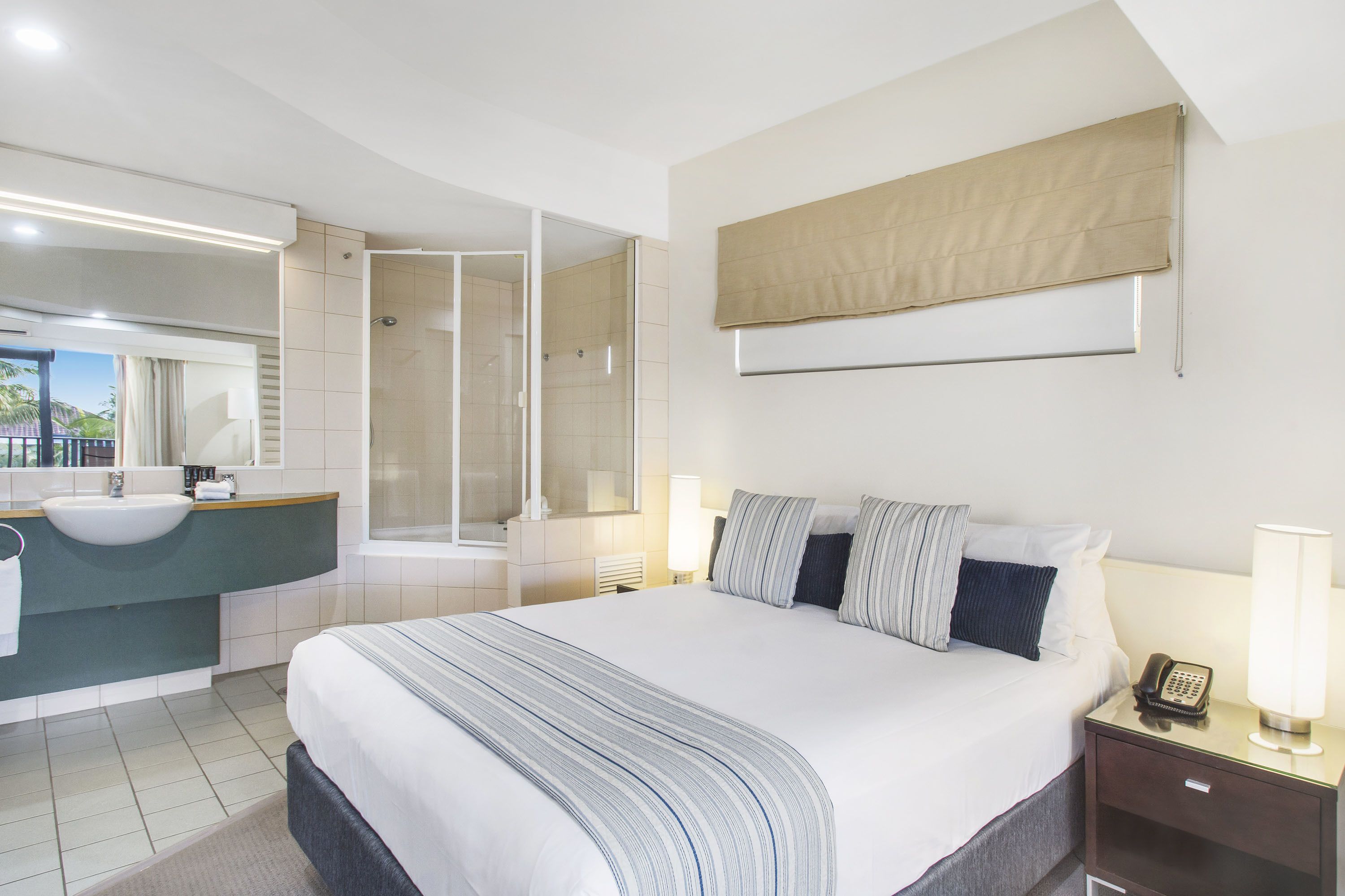 A hotel room with a large bed, a bathroom with a sink and mirror, and a shower.