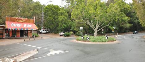 A street corner with a surf hire shop, a roundabout, and a tree in the center.