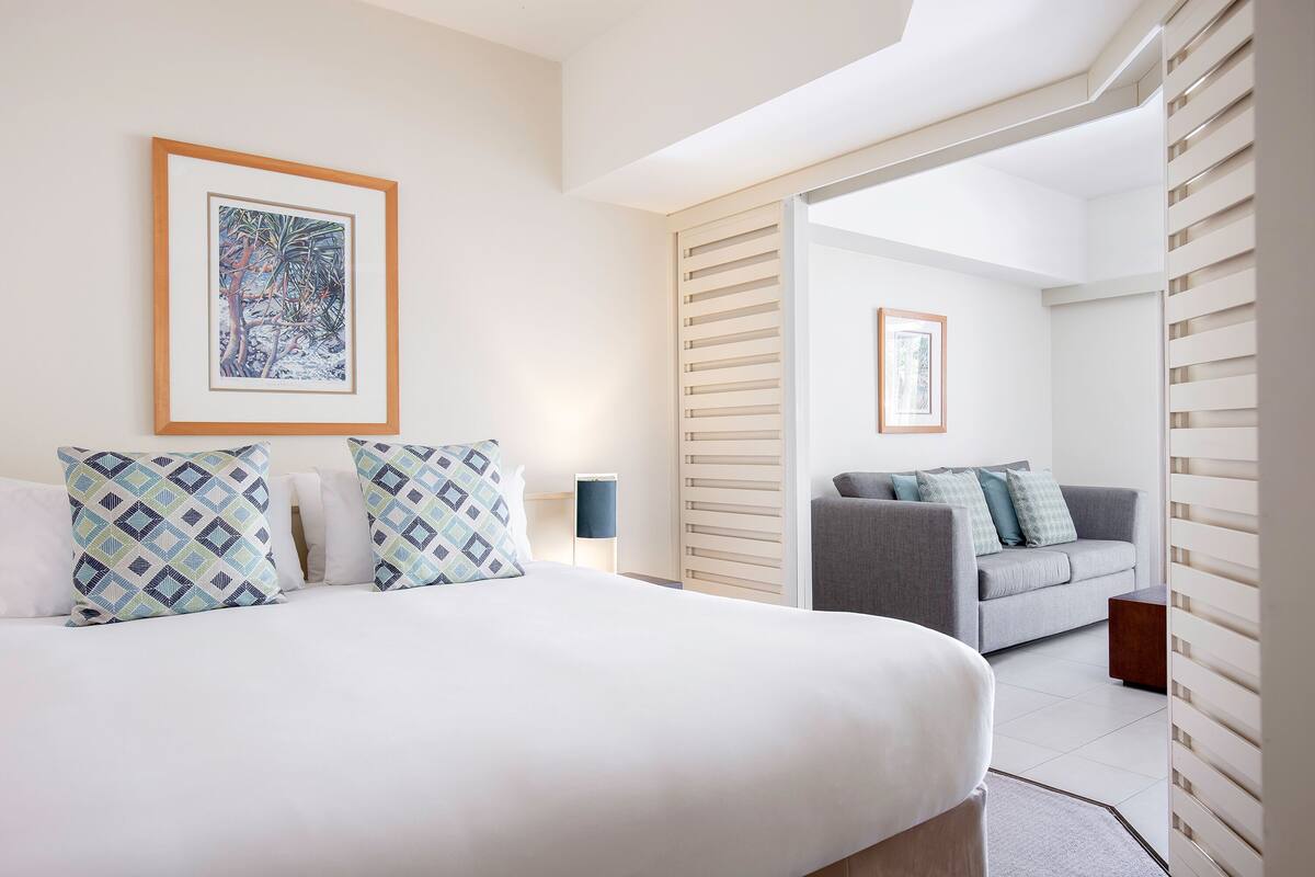 Een moderne hotelkamer met een bed, een grijze bank, een inlijsting kunstwerk aan de muur, en een houten lattenwand.