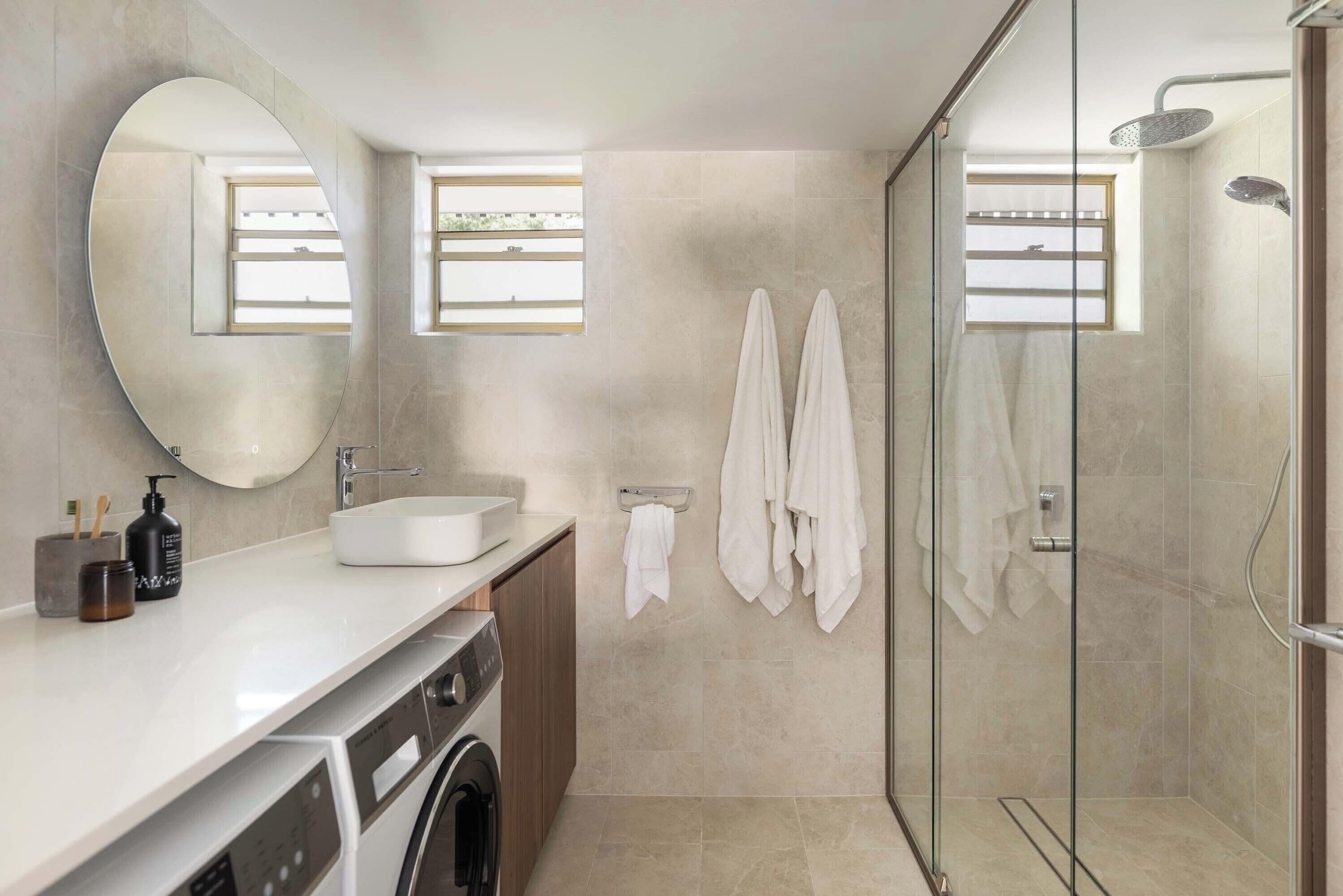 A modern bathroom with a large mirror, a sink, a glass-enclosed shower, and a washing machine.