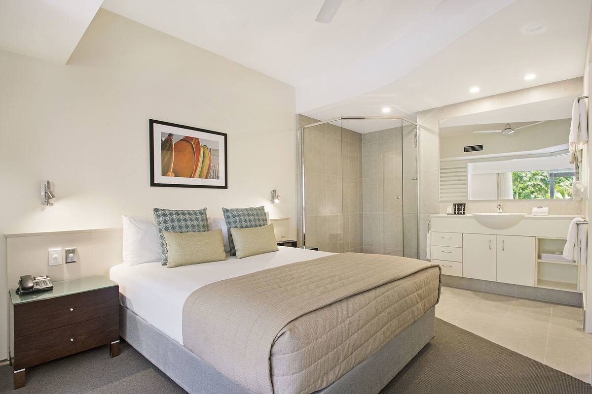 Hotelkamer met een bed, nachtkastje met telefoon, douche, badkamer met wastafel en spiegel, en een lijst aan de muur.