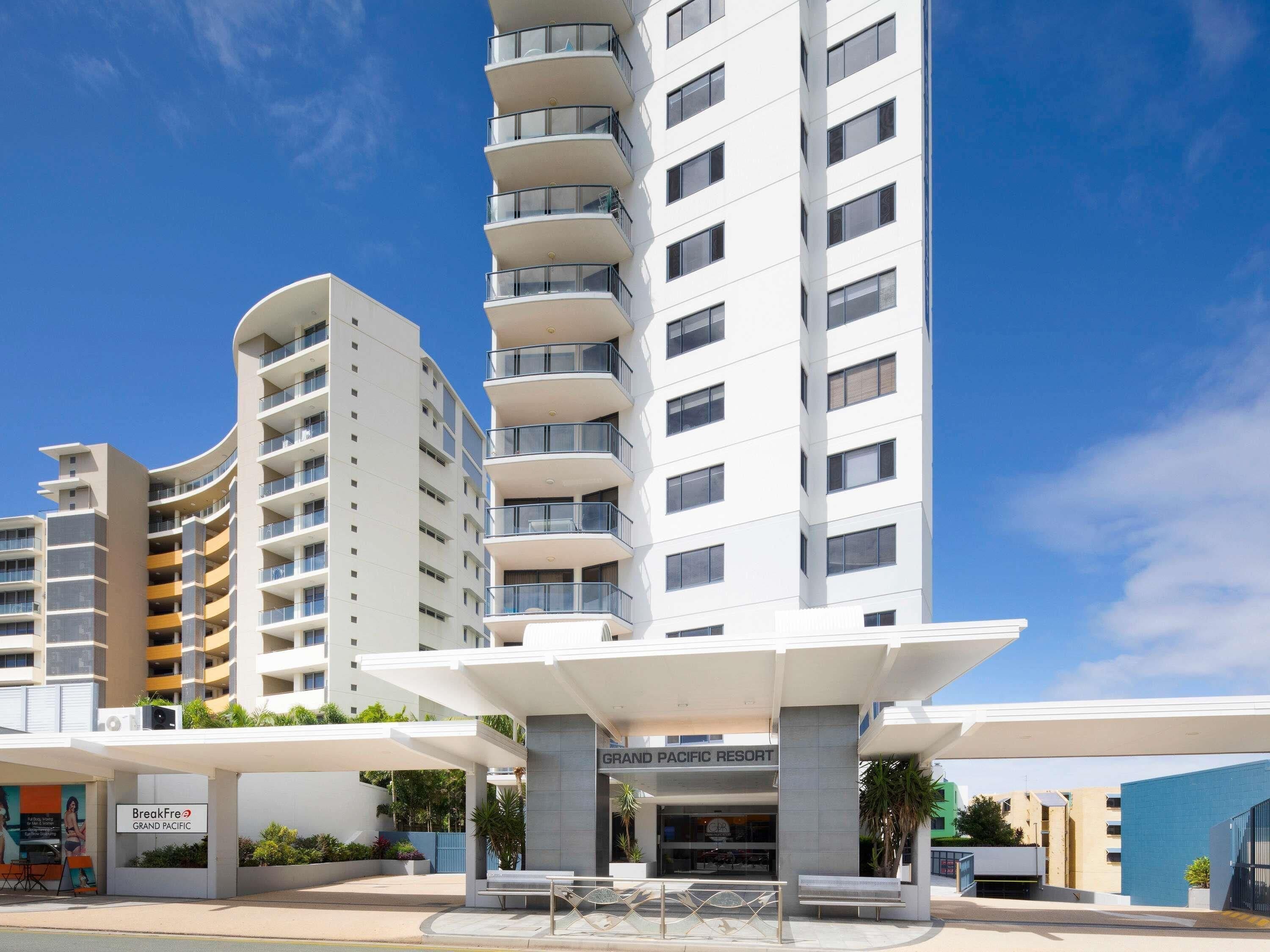 A modern hotel with a prominent entrance, multiple balconies, and a clear sky.