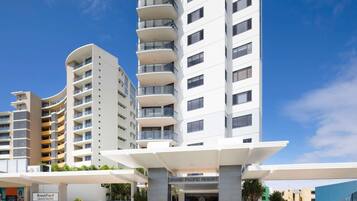 A modern hotel with a prominent entrance, multiple balconies, and a clear sky.