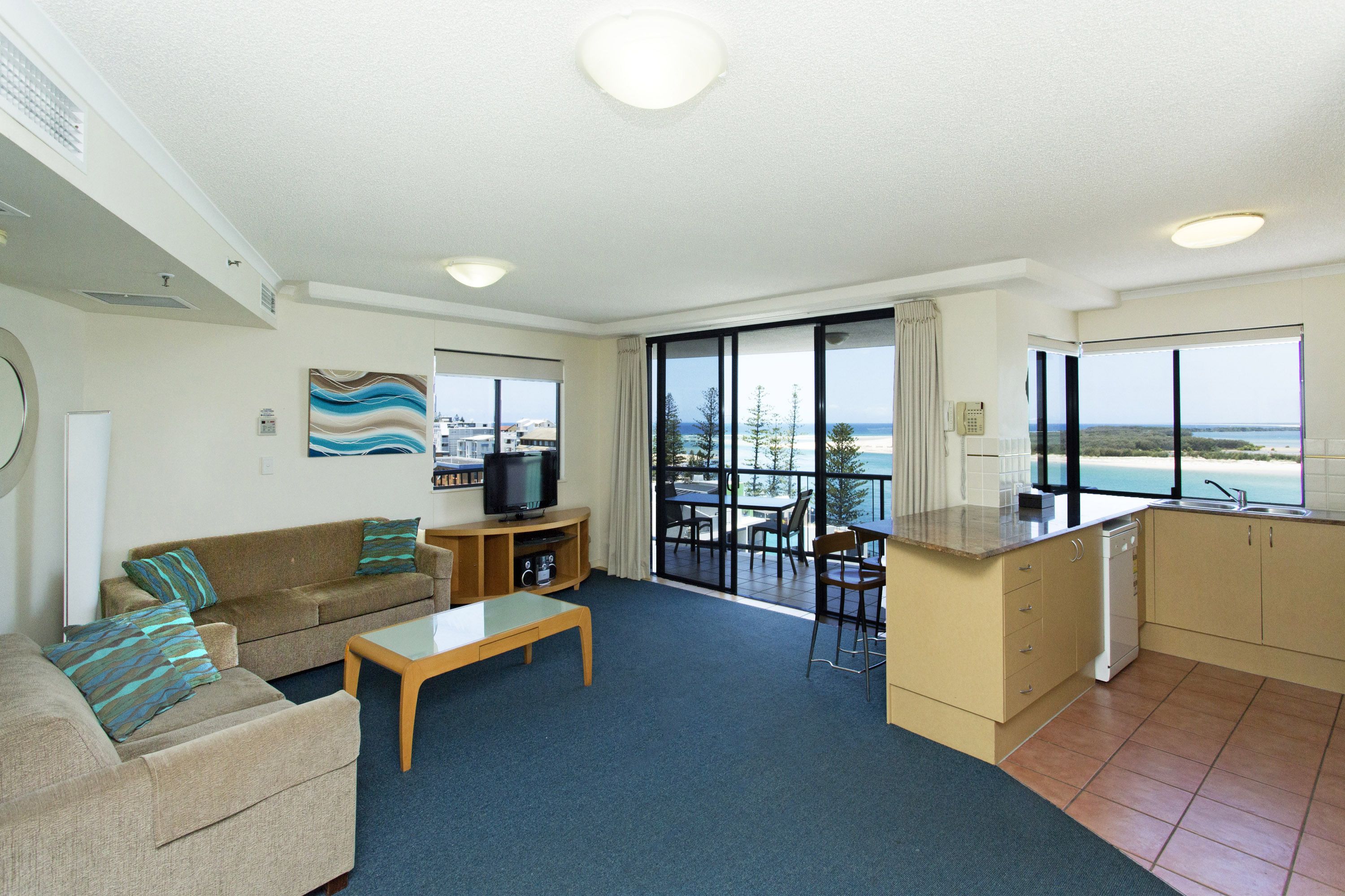 Een moderne woonkamer met een bank, salontafel en televisie. Het heeft een balkon met uitzicht op zee.