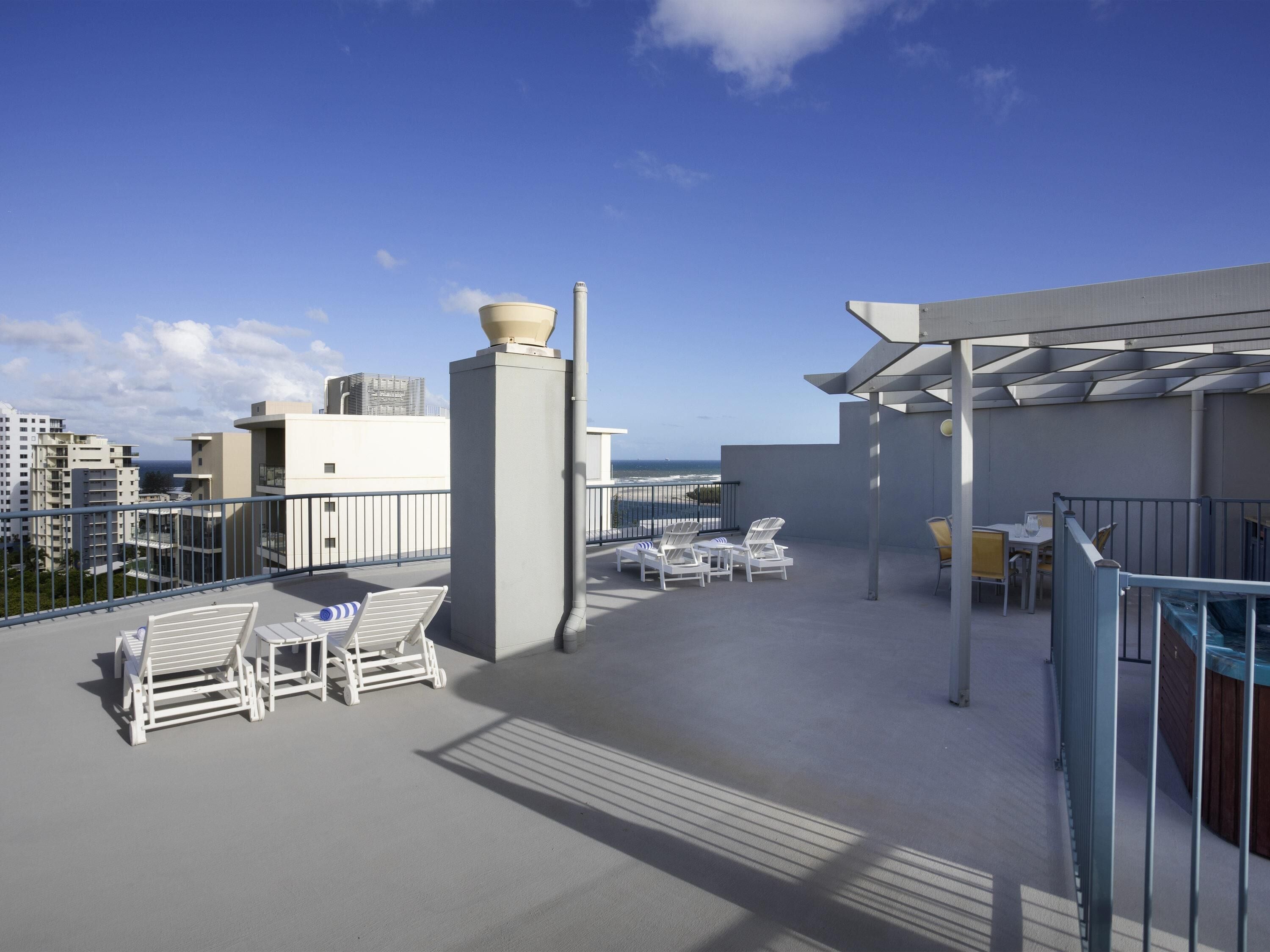 A rooftop terrace with lounge chairs, a pergola, and a view of the ocean.