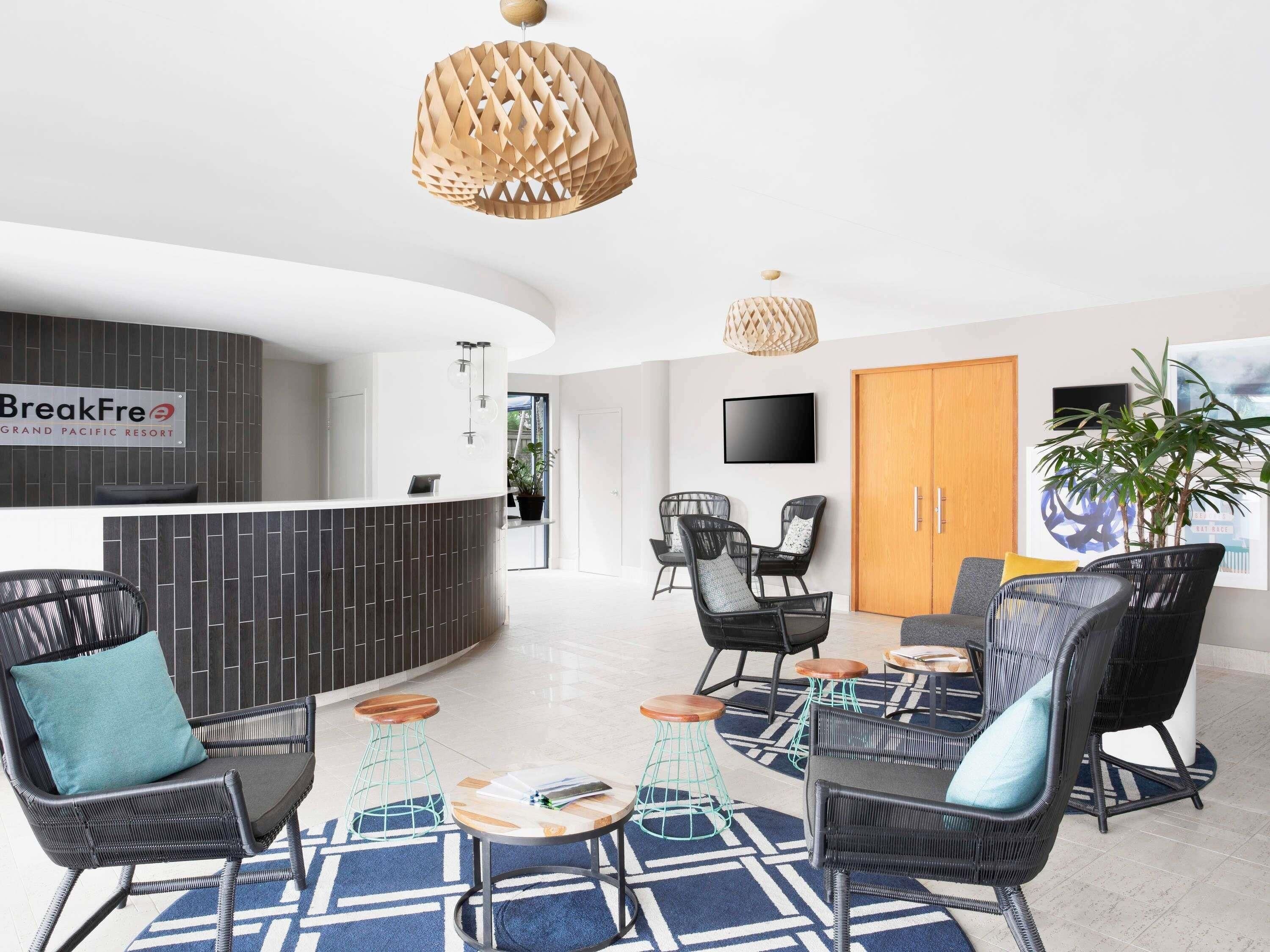 A modern reception area with a reception desk, black wicker chairs, a coffee table, and a large potted plant.
