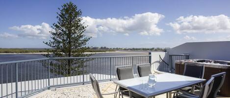 A balcony with a table and chairs, overlooking a body of water and a distant shoreline.
