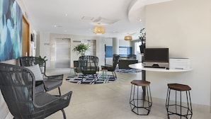 A modern hotel lobby with black wicker chairs, a reception desk, a large screen, and a printer. - BreakFree Grand Pacific Resort (Caloundra)