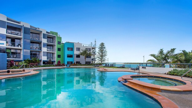 A swimming pool with a curved design, surrounded by a multi-story building with balconies. - BreakFree Grand Pacific Resort (Caloundra)
