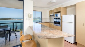 A modern kitchen with a large island, a microwave, and a refrigerator. There is a balcony with a view of the sea. - BreakFree Grand Pacific Resort (Caloundra)