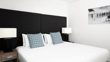 Habitación de hotel con una cama grande, dos mesitas de noche con lámparas, un cabecero negro y un cuadro colgado en la pared.