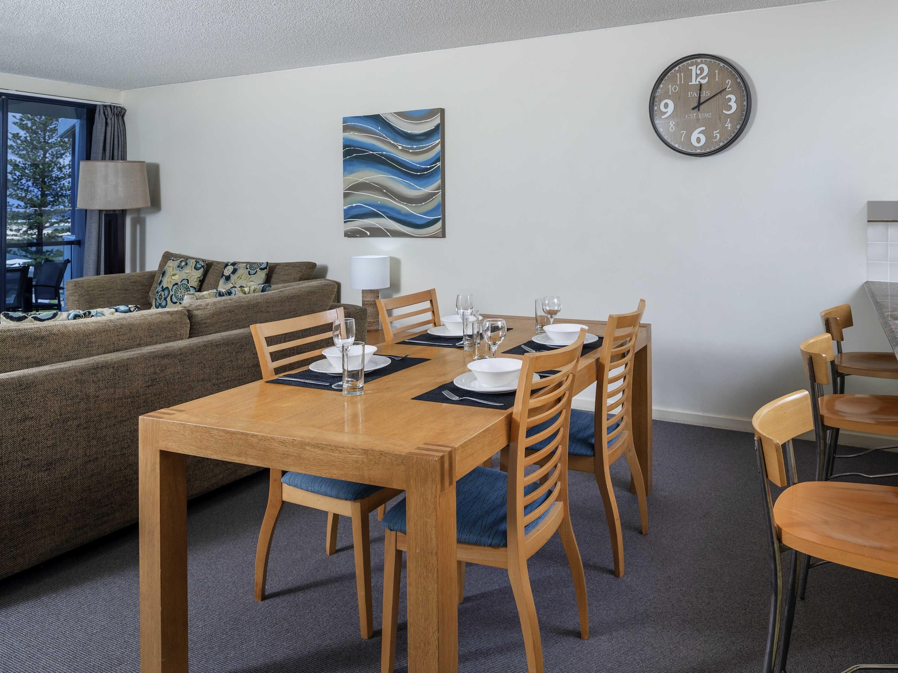 A modern living room with a dining area, a sofa, a clock, and a painting on the wall.