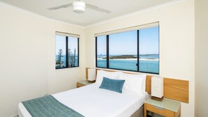 A hotel room with a large bed, a nightstand, a bedside table, and a view of the sea. - BreakFree Grand Pacific Resort (Caloundra)