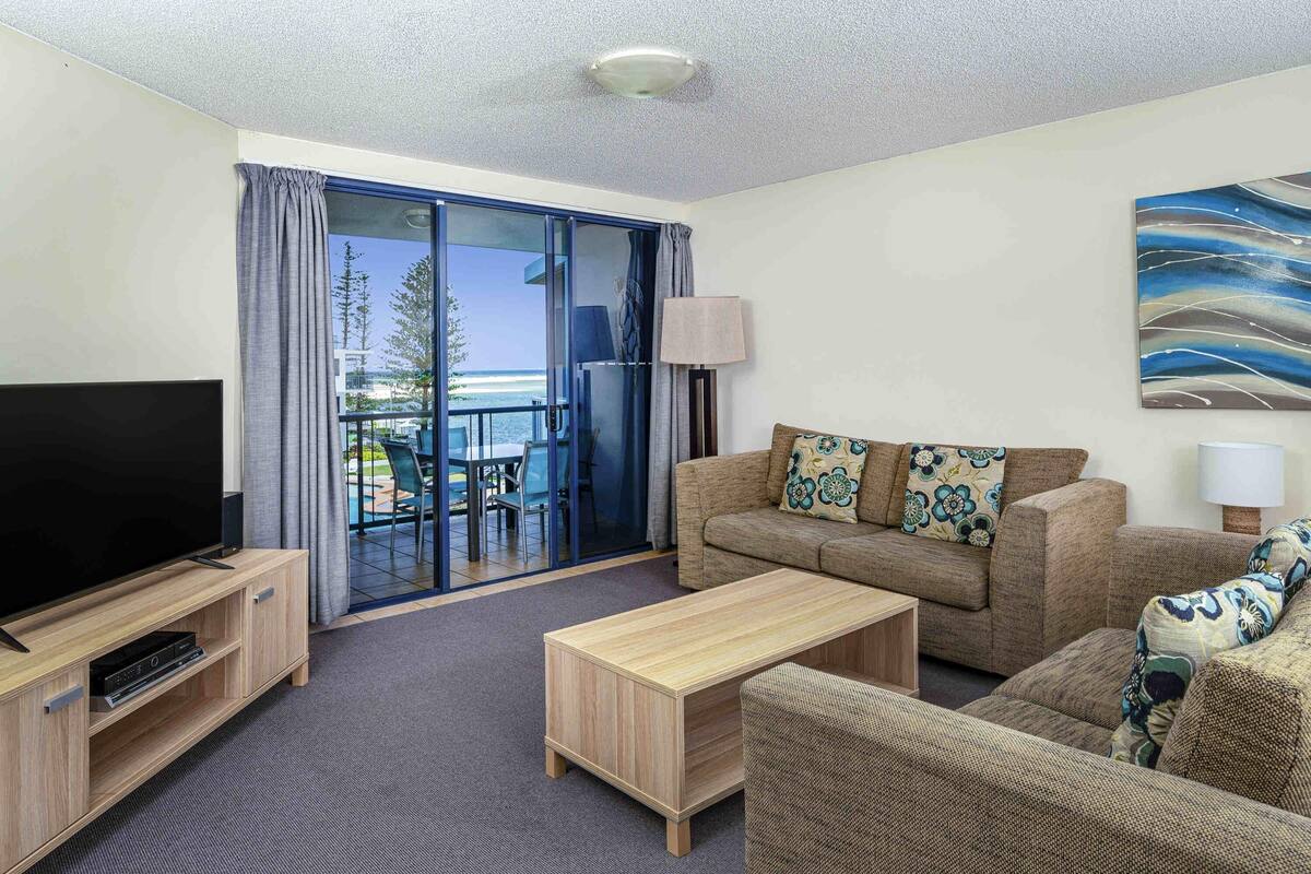 A hotel room with a TV, sofa, coffee table, and a balcony with a view.