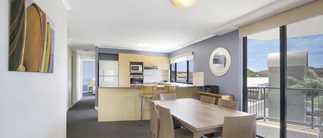 A modern hotel room with a dining area, kitchenette, and a balcony with a view.