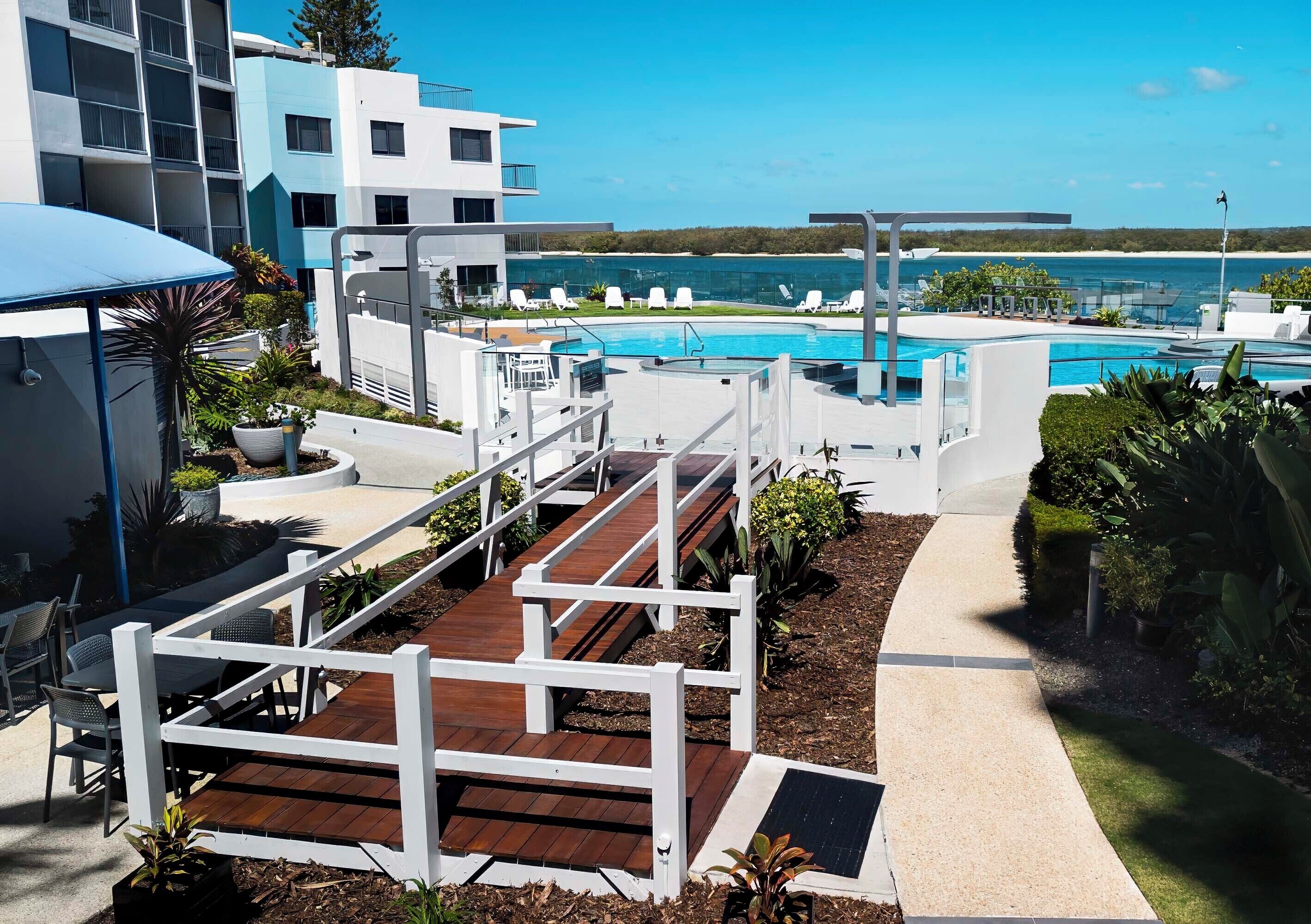 Un hotel moderno con zona de piscina, mobiliario exterior y vista al mar.