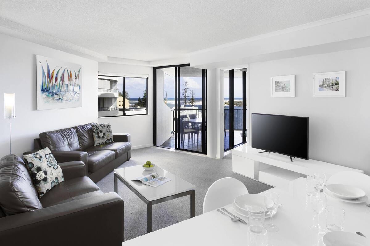 A modern living room with a sofa, coffee table, dining table, and TV.