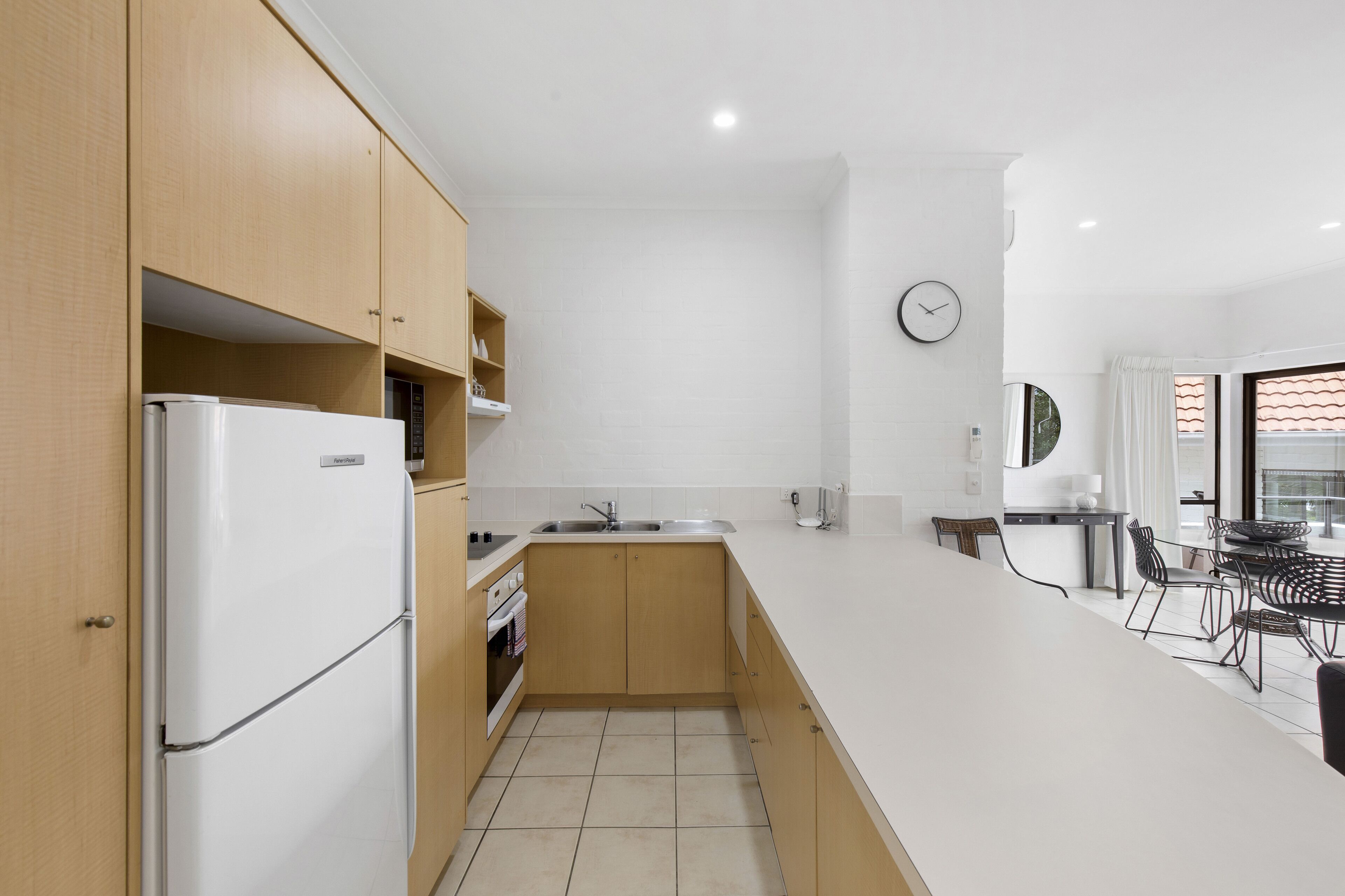 A modern kitchen with wooden cabinets, a white refrigerator, a sink, and a dining area with a table and chairs.