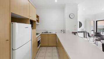 A modern kitchen with wooden cabinets, a white refrigerator, a sink, and a dining area with a table and chairs.